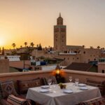 Vista panoramica dei tetti di Marrakech con la Koutoubia sullo sfondo e tavoli apparecchiati su un rooftop